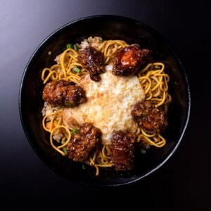 A delicious close-up of fried egg on noodles with spicy chicken in a dark setting.