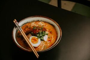 Close-up of gourmet ramen with egg and fresh greens in a bowl with chopsticks.
