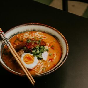 Close-up of gourmet ramen with egg and fresh greens in a bowl with chopsticks.