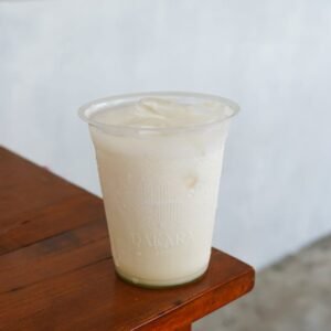 A refreshing iced creamy drink in a clear plastic cup on a wooden table.