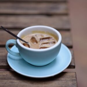 Iced coffee served in a blue cup on a rustic wooden table outdoors.
