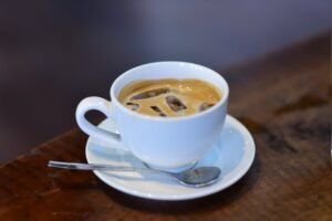 Iced espresso in a white cup with saucer and spoon on rustic wooden table.