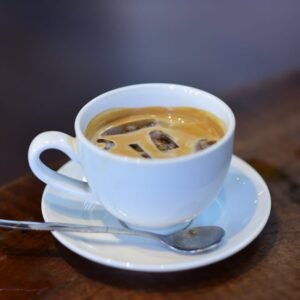 Iced espresso in a white cup with saucer and spoon on rustic wooden table.