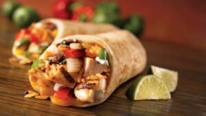 Close-up of a savory chicken burrito with fresh lime wedges, showcasing vibrant Mexican ingredients.